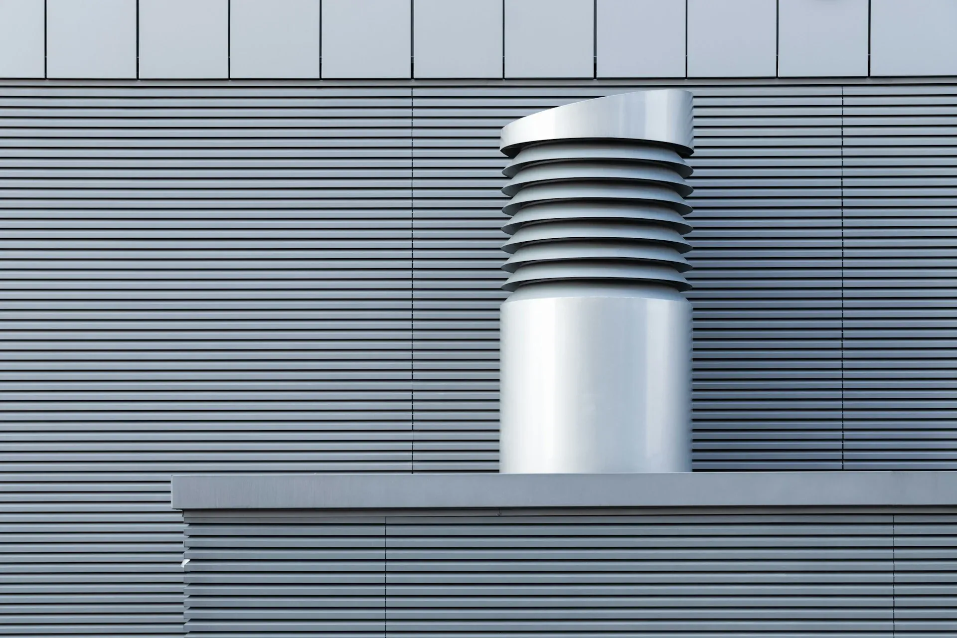 Metal exhaust vent above a ribbed industrial facade